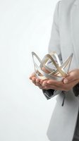 Caucasian male professional in light gray business suit holding abstract metallic sculptural object with interlocking curved bands in hands against white background for corporate concepts.