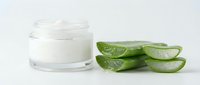 Natural aloe vera gel in glass jar with fresh cut leaves for skincare and cosmetic treatments on white background.