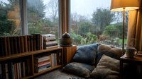 Cozy reading nook with built-in bookshelf, comfortable cushions and warm lighting by large window overlooking garden. Perfect for relaxation and home decor.