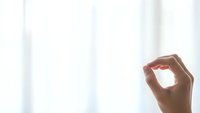 Woman hand making OK gesture against bright window light creating silhouette effect in minimalist interior space for positive communication concepts.