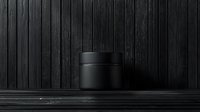 Minimalist black cosmetic jar on dark wooden background with dramatic lighting and shadow play. Luxury skincare packaging concept for premium products.