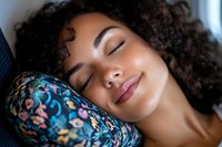 Young African American woman with curly hair sleeping peacefully on floral pillow, expressing serenity and relaxation in natural light setting. Perfect for wellness and lifestyle content.