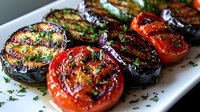 Grilled eggplant slices and tomatoes garnished with fresh herbs and seasonings on white plate, showcasing charred vegetables with appetizing grill marks and glossy finish.