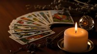 Mystical tarot cards spread on wooden table with burning candle and crystal ball creating atmospheric fortune telling scene for spiritual guidance.