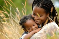 African American mother and young son share tender moment outdoors among tall grass during golden hour, expressing pure joy and maternal love.
