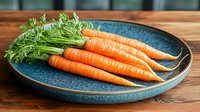 Fresh organic carrots with green tops on blue ceramic plate against wooden background, raw vegetables for healthy cooking and farm market produce.