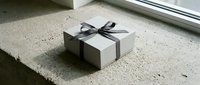 Elegant white gift box with dark ribbon bow sitting on concrete surface near window with natural lighting for special occasions and celebrations.