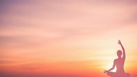 Silhouette of woman practicing yoga meditation pose against vibrant sunset sky with pink orange gradient colors for wellness mindfulness content.