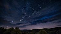 Orion constellation glowing bright in starry night sky above silhouetted forest landscape with wispy clouds for astronomy and celestial navigation themes.