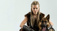 Young woman with blonde braided hair and dark warrior-style clothing posing with German Shepherd dog on white background for character design and fantasy projects.
