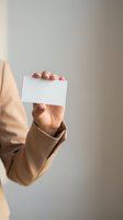 Professional woman hand holding blank white business card mockup in beige blazer for corporate branding and marketing design templates.