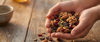 Hands holding mixed nuts and dried fruits on rustic wooden table. Healthy snacking, organic food ingredients for cooking and baking recipes.