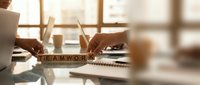 Business teamwork concept with wooden letter blocks spelling teamwork on desk with hands typing on laptop in modern office environment.