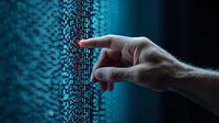 Male hand pointing at glowing digital binary code wall in dark blue technological environment, representing cybersecurity and data interaction concepts.