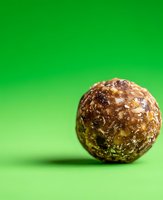 Chocolate truffle with golden sparkles and nuts on vibrant green background. Macro food photography with selective focus and soft shadow effect.