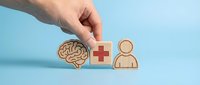 Hand arranging wooden icons of brain, medical cross, and person on blue background, representing mental health care, psychology services, and healthcare support.