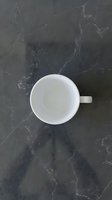 Empty white ceramic mug on dark marble surface with veining, overhead view. Suitable for beverage, kitchen, and tableware design projects.