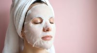 Young woman with white towel on head applying hydrating face mask for skincare routine and spa treatment at home.