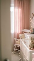 Cozy nursery room with white wooden crib, rocking chair, soft pink curtains and teddy bears creating warm atmosphere for baby care and parenting.