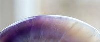 Polished amethyst crystal sphere with translucent purple and white banding, displaying natural striations and light refraction for mineral collection, jewelry design, and wellness product marketing.