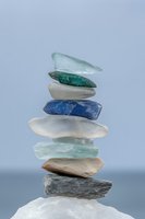 Balanced stack of colorful sea glass and smooth stones creating zen tower against soft blue background for meditation and wellness concepts.