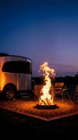 Travel trailer camping scene with roaring campfire at twilight creating cozy outdoor adventure atmosphere for recreational vehicle enthusiasts and nature lovers.