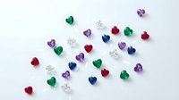 Colorful heart-shaped gemstones and diamonds scattered on white background. Mixed precious stones in red, blue, green, purple hues for jewelry design.