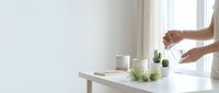 Modern minimalist home office workspace with white desk, laptop, plant and hands reaching for coffee cup in bright natural light interior.