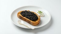 Gourmet toast topped with black caviar served on white plate with cream cheese and microgreens, luxury seafood appetizer for fine dining and culinary concepts.