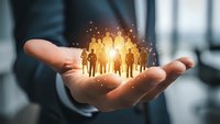 Businessman holding glowing group of people silhouettes in cupped hands representing team management, human resources and leadership concepts.