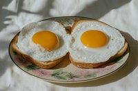 Two sunny side up fried eggs on toasted bread slices served on a floral plate, morning breakfast concept with natural sunlight shadows.