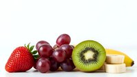 Fresh mixed fruits including strawberry, red grapes, sliced kiwi and banana pieces arranged on white background for healthy eating and nutrition concepts.