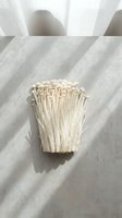 Enoki mushrooms arranged on neutral linen fabric with natural sunlight casting dramatic shadows, suitable for food styling and culinary content.