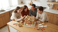 Family of four decorating gingerbread house together in bright kitchen during holiday season. Multigenerational group enjoying festive baking activity with candies and icing.