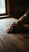 Male hands resting on wooden table near window with natural light, conveying contemplation, rest, or emotional moment. Suitable for wellness, mental health, lifestyle, and editorial content.