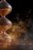 Flowing golden sand particles from hourglass creating magical dust effect against dark background, with soft bokeh lights and dramatic atmosphere.