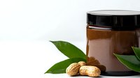Isolated jar of organic peanut butter with fresh peanuts and green leaves on white background, ready for food packaging, recipe blogs, and nutritional product marketing.