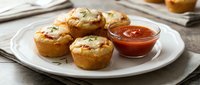 Golden baked egg muffins with cheese and herbs served on white plate with tomato sauce dip, healthy breakfast or brunch meal on wooden table background.