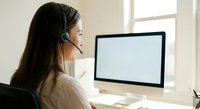 Professional young woman with headset working at computer in modern office environment for customer service and remote work applications.
