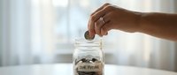Woman's hand dropping coin into glass jar labeled Our Future, symbolizing savings, financial planning, and investment goals.