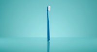 Blue toothbrush standing upright on turquoise background with reflection. Clean dental hygiene tool for oral care and teeth cleaning routine.