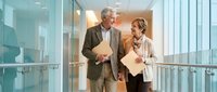 Senior business professionals walking in modern office corridor discussing documents and strategy for corporate meeting.