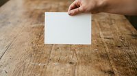 Person of indeterminate ethnicity holding blank white card on rustic wooden surface for mockup, branding, or marketing material presentation.