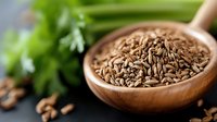 Organic cumin seeds in wooden spoon with fresh celery and herbs in background, macro food photography for cooking blogs and culinary websites.