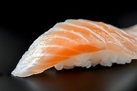 Fresh salmon nigiri sushi piece on dark background, selective focus on raw fish texture showing delicate marbling and expert knife cuts, traditional Japanese cuisine.