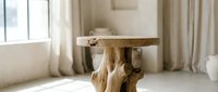 Rustic handcrafted wooden side table with natural tree root base in a bright minimalist interior with soft neutral tones and linen curtains.