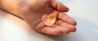 Open palm holding glowing orange heart symbol representing love, care, compassion and emotional wellness in warm lighting for healthcare concepts.
