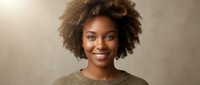 Young African American woman with curly afro hair smiling warmly in cozy brown sweater against neutral background for lifestyle and portrait photography.