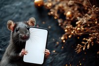 Gray rat holding blank smartphone screen with tiny paws against dark background with golden bokeh lights and dried flowers, mockup for app or mobile design.