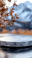 Marble podium display with autumn branches and snowy mountain backdrop, featuring brown leaves and blurred winter landscape for product presentation.